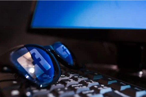 lunettes noires posées sur le clavier d’un ordinateur dont les verres reflètent le logo de facebook